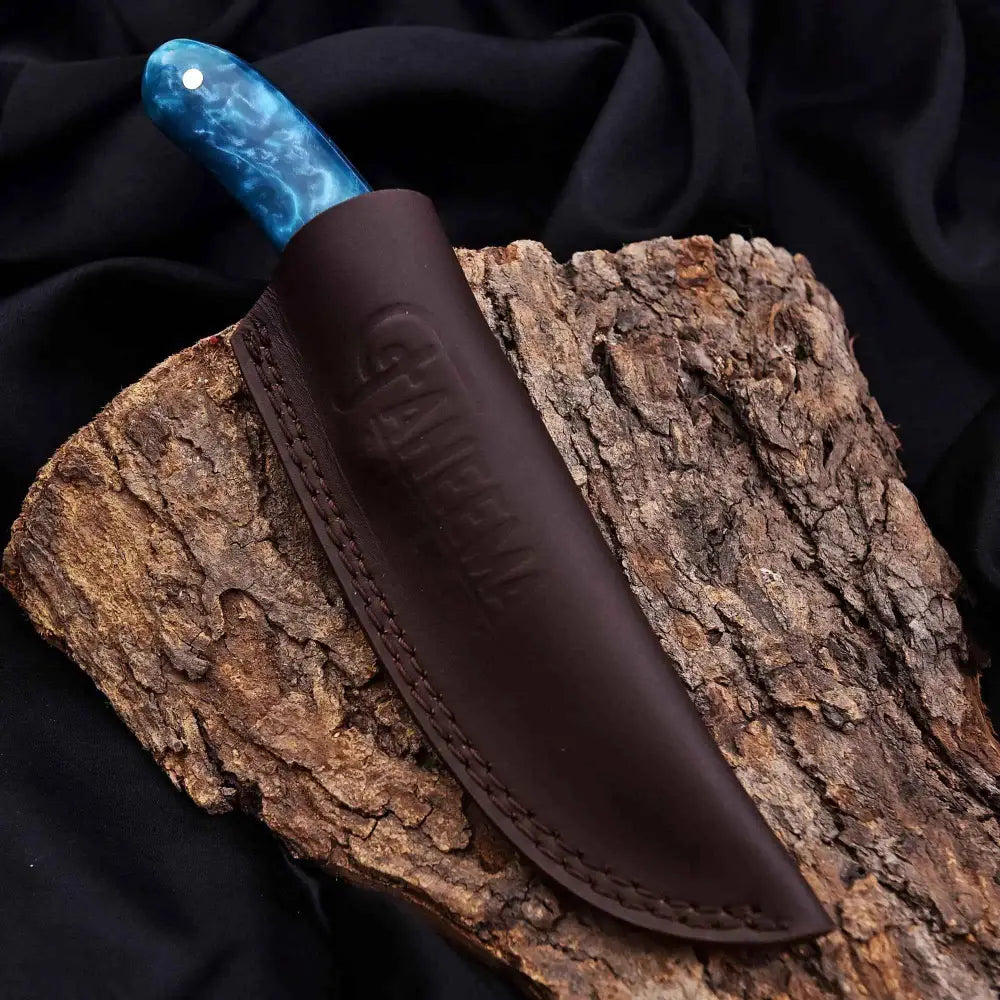 Blue marbled turquoise outdoor knife with leather sheath on tree bark