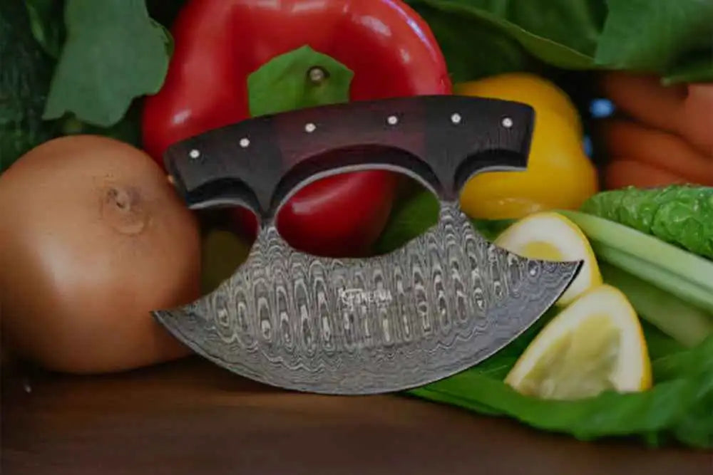 A curved, damascus steel knife with a dark wooden handle and silver-toned blade pattern rests among fresh vegetables.