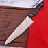 Damascus chef knife with gold silver patterns and black handle on wood board
