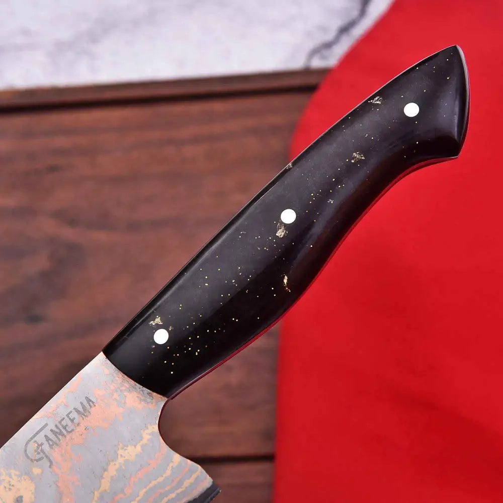 Damascus chef knife with black handle, gold flecks, white inlays, and Faneema engraving