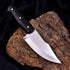 Black-handled sooty outdoor knife with polished stainless steel blade on tree bark