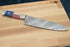 Faneema Cutlery Texas Damascus steel knife chef knife with a patterned blade and Texas flag handle on wooden cutting board